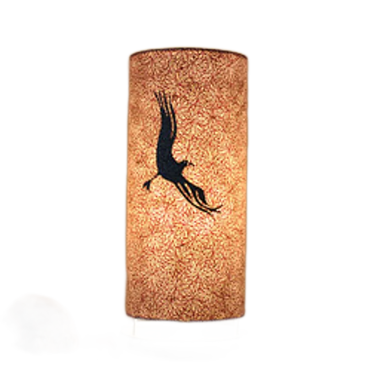 Une lampe de table cylindrique allumée, dont l'abat-jour texturé est décoré de la silhouette sombre d'un oiseau déployant ses ailes, posée sur une surface en bois à côté d'une pierre claire.