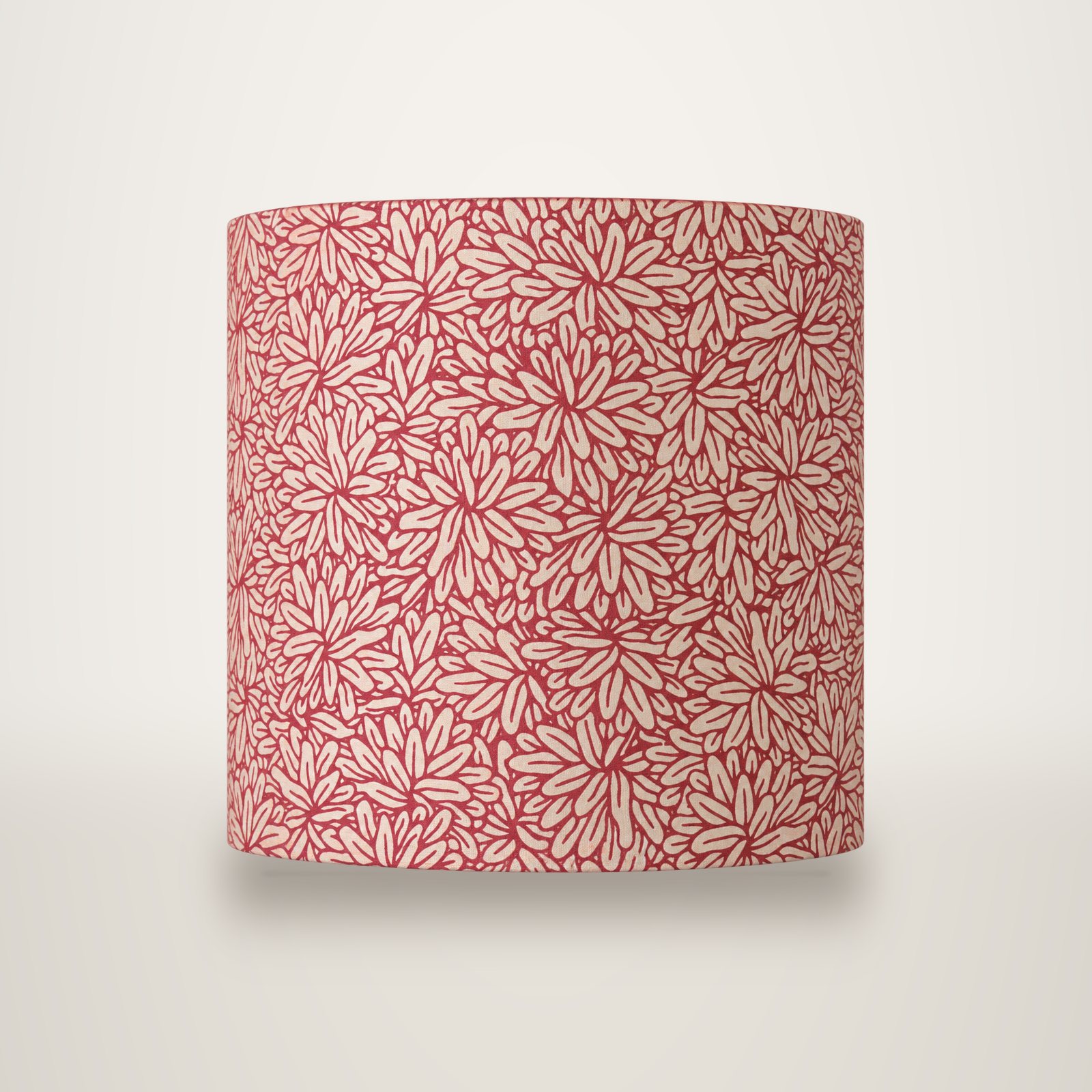 Gros plan d'un motif de fleurs stylisées beiges sur un fond rouge framboise, probablement un tissu ou un papier peint.