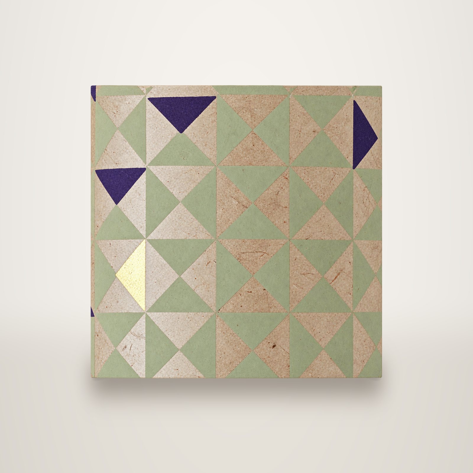 Gros plan sur un papier décoratif à motif de triangles vert sauge et kraft, avec quelques triangles violets et un triangle doré.